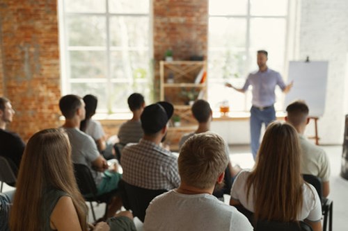 A group of adults sat together being spoken to by a teacher.